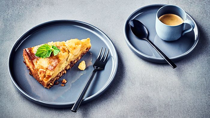 A slice of apple cake on a grey plate with a cup of coffee.